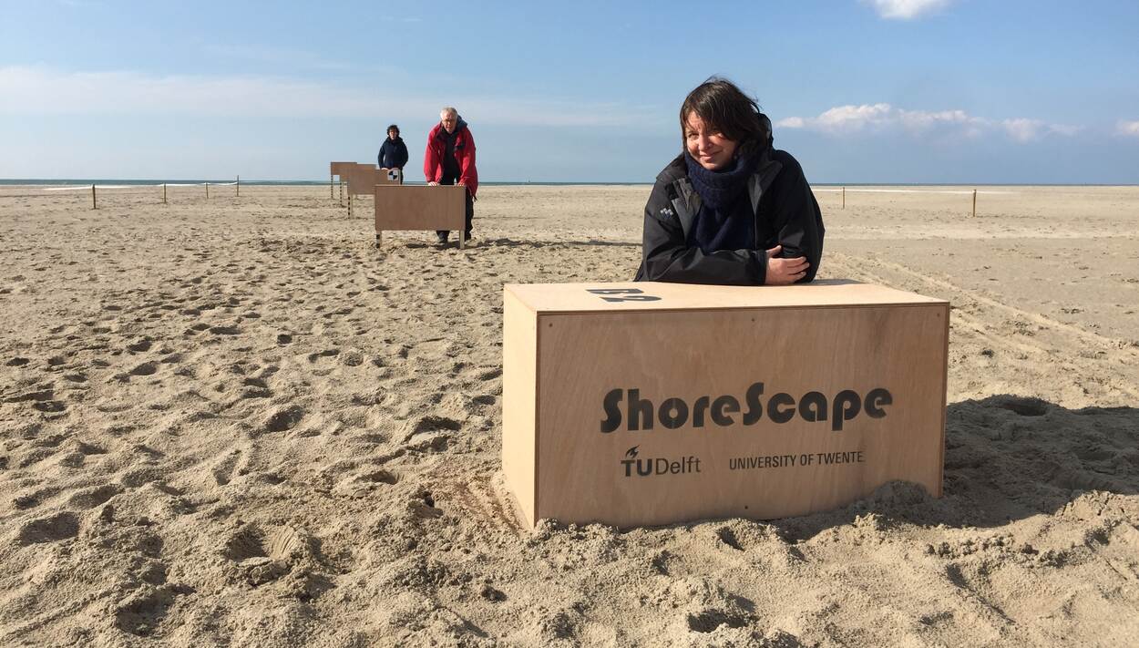 Vrouw op strand met houten doos waarop ShoreScape staat.