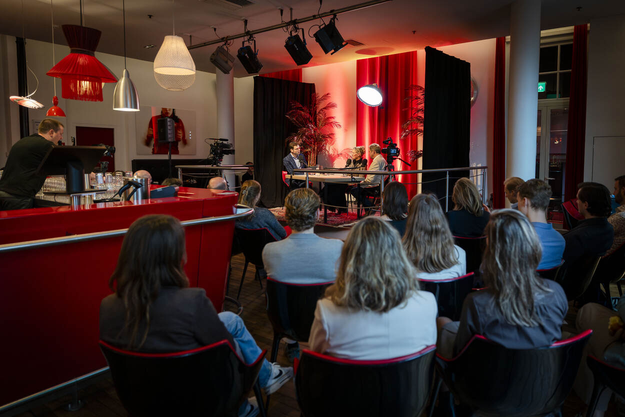 Zaal met mensen die luisteren naar een gesprek tussen drie mensen