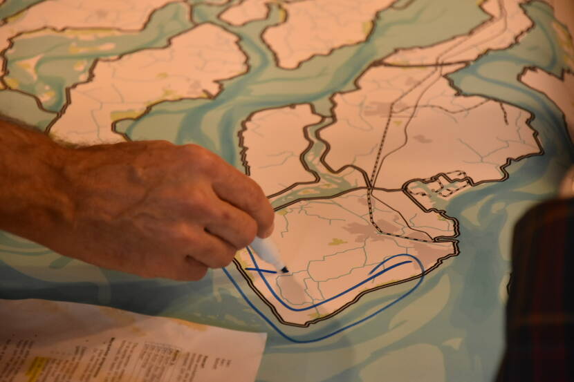 Een close-up van een stuk van de kaart van Nederland. Daarboven zweeft een hand die een stift vasthoudt en een gedeelte op de kaart omcirkelt.