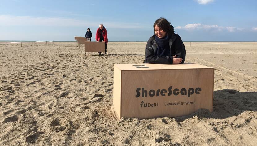 Vrouw op strand met houten doos waarop ShoreScape staat.