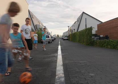 Spelende kinderen met een oranje bal in een woonwijk in Noord-Brabant. In de straat een afvoergoot met water.