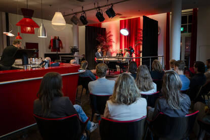 Zaal met mensen die luisteren naar een gesprek tussen drie mensen